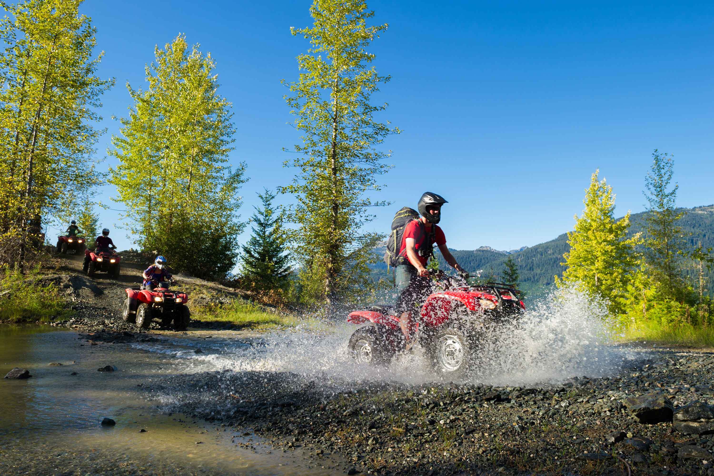 Adventurers crossing small river in the woods on red ATVs