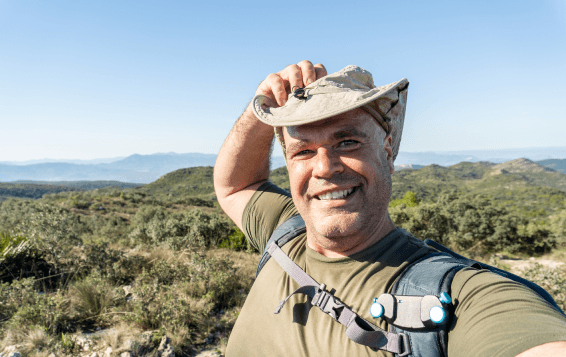 Man in hiking gear smiling and adjusting hat against mountain landscape